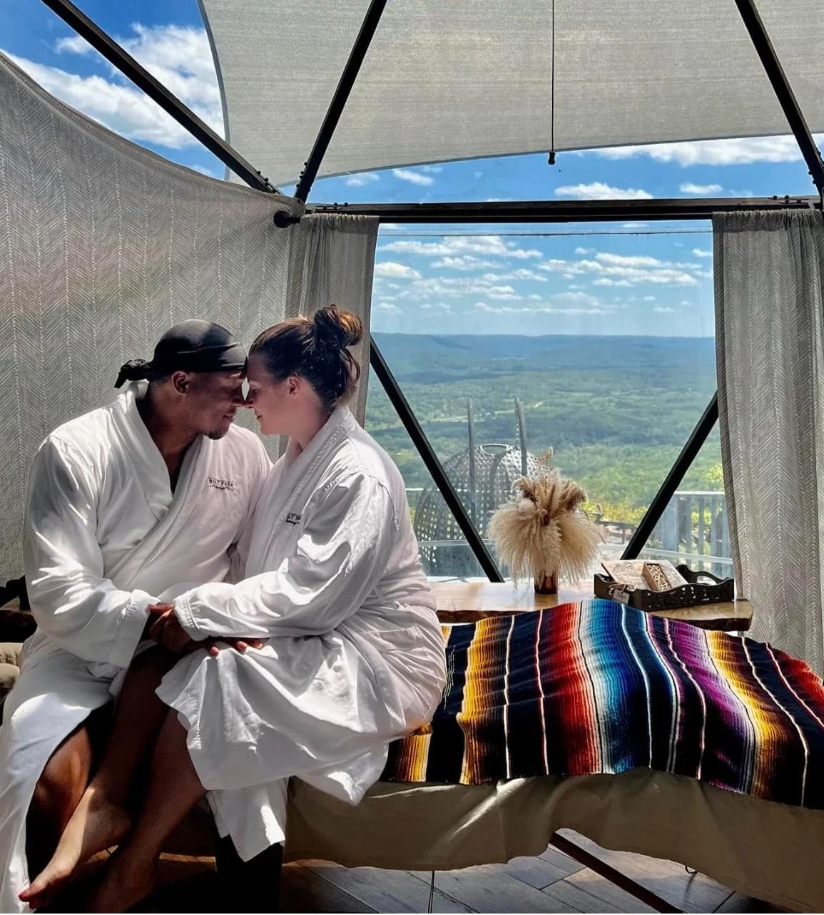 Two guests in robes beside a massage setup with a mountain view.